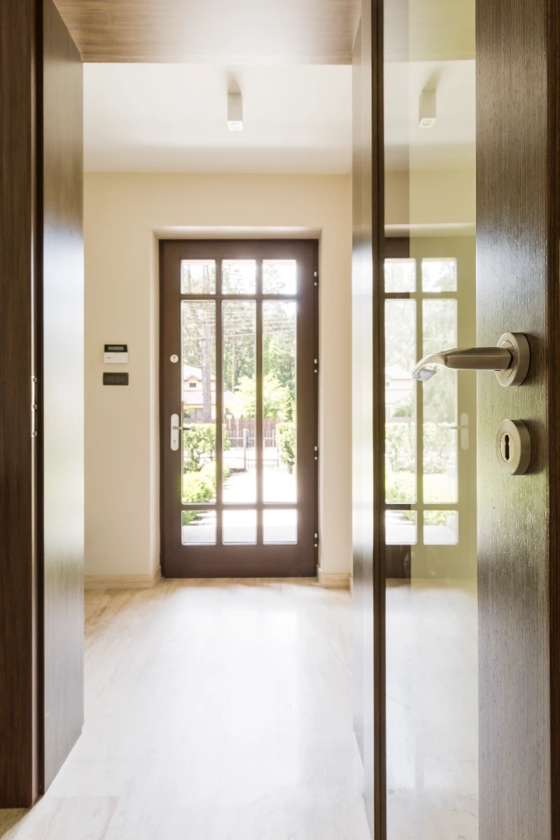Nowoczesne drewniane drzwi wejściowe z przeszkleniami i chromowanym uchwytem w jasnym holu