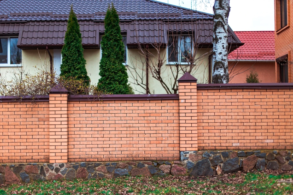 Ogrodzenie z bloczków z ceglanym murem i kamienną podmurówką przed domem