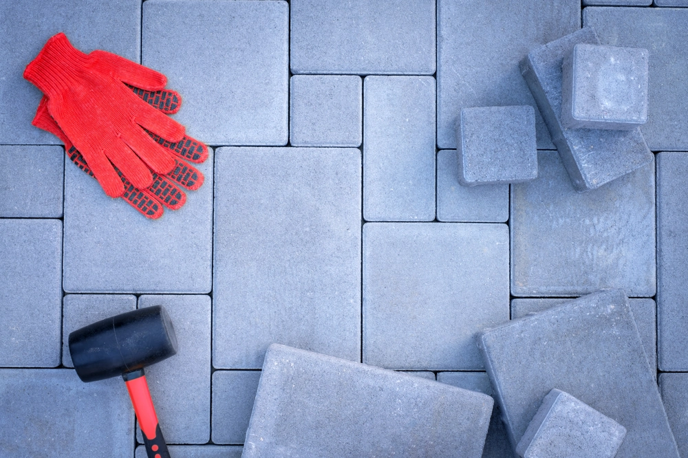 Układanie kostki brukowej: gumowy młotek, czerwone rękawice i szare brukowe płyty