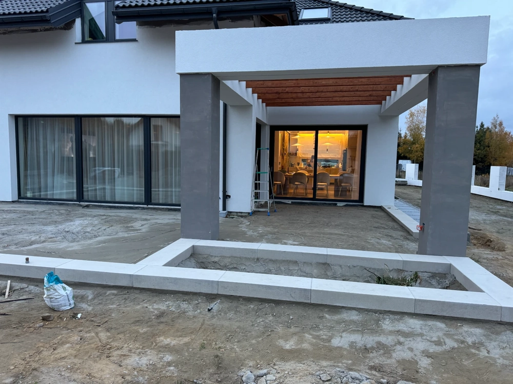 Przygotowanie podbudowy tarasu z betonowymi obrzeżami i drewnianą pergolą przy nowoczesnym domu