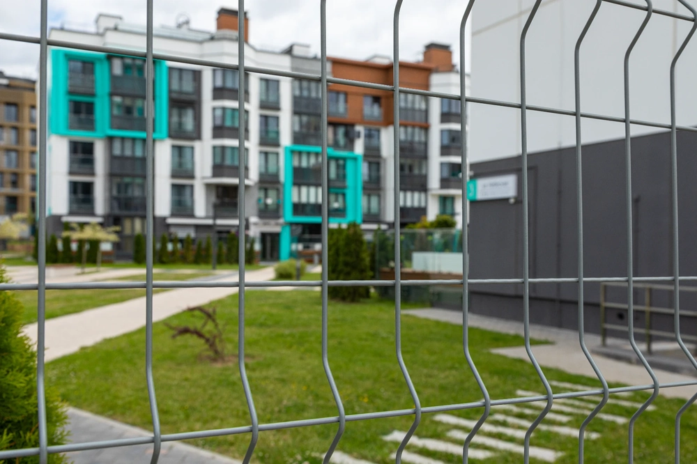 Ogrodzenia panelowe na granicy zielonego podwórka, w tle nowoczesne budynki wielorodzinne
